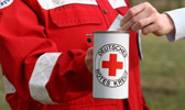 Foto: Eine Hand steckt einen Geldschein in eine Spendendose mit Rotem Kreuz.